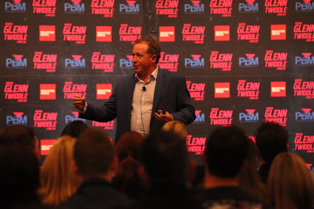 Luke Anderson speaking on stage to a real estate audience